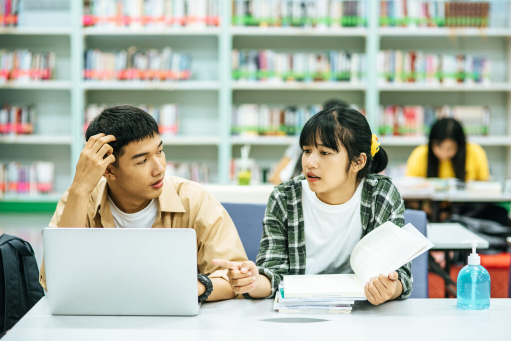 Women read books and men use laptops to search for books in libr