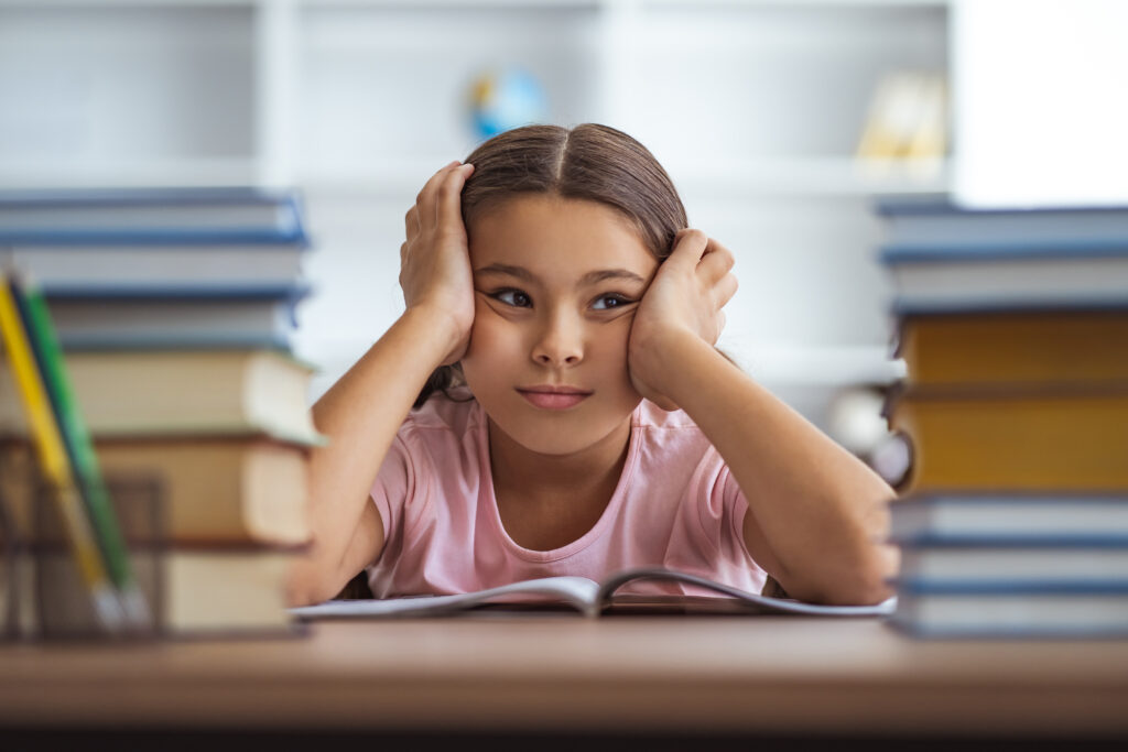 The tired schoolgirl sitting at the desk with books